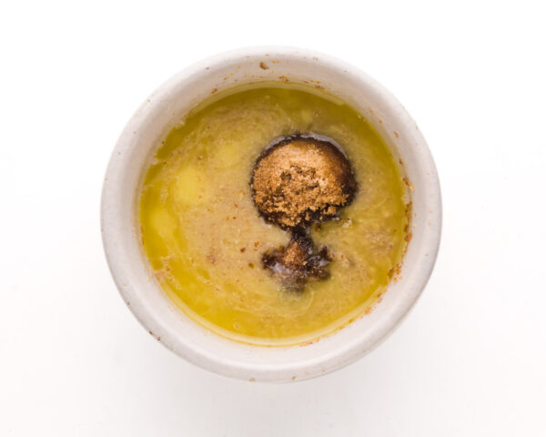Brown sugar is seen poking through melted vegan butter in a bowl.