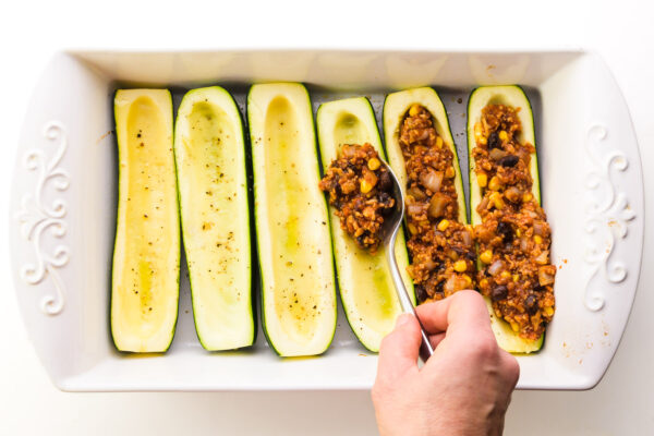 Zucchini boats are being filled with veggie filling.