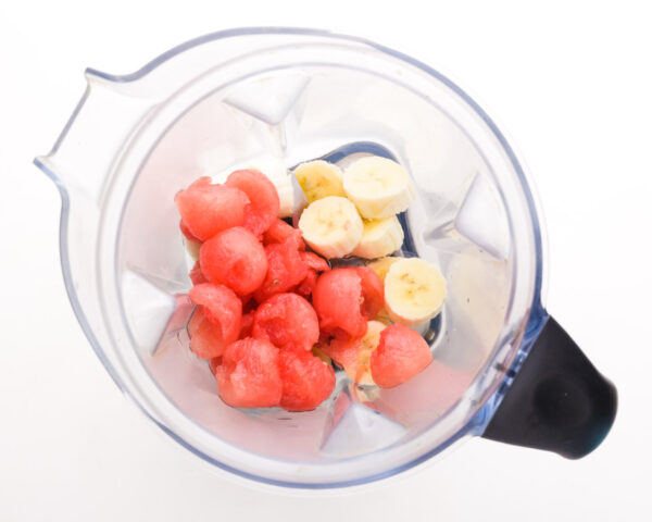 Fresh fruit is in a blender with protein powder and other smoothie ingredients.