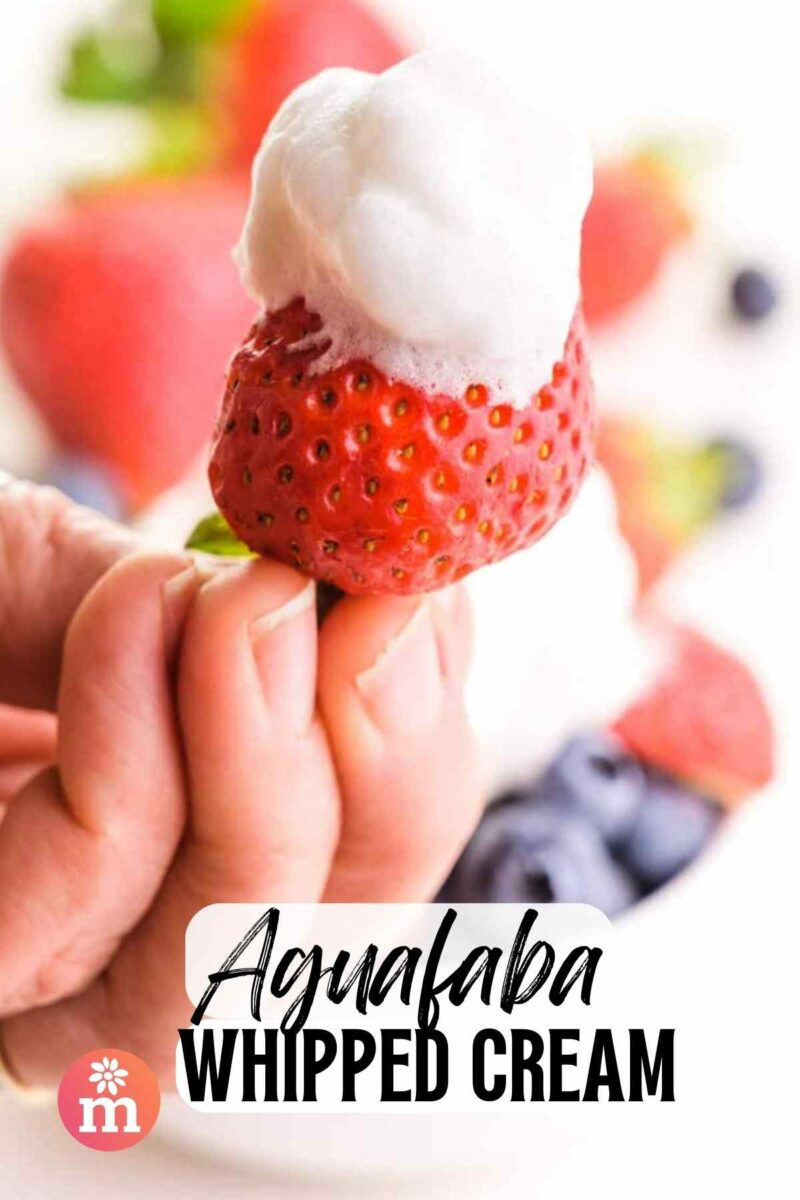 A hand holds a strawberry with whipped cream on top. The text reads, Aqufaba Whipped Cream.