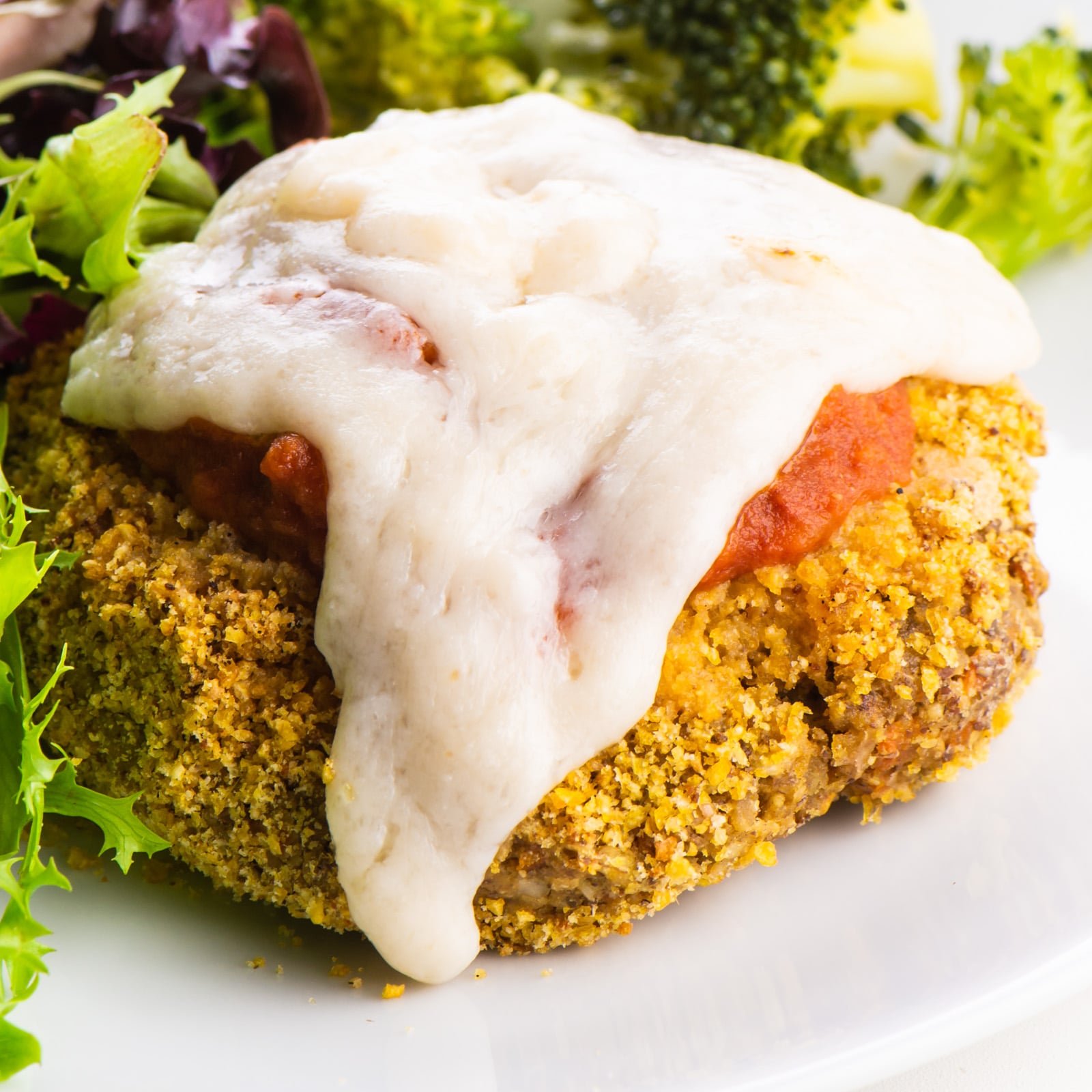 A closeup of a vegan chicken parmesan patty with marinara sauce and melted cheese on top.