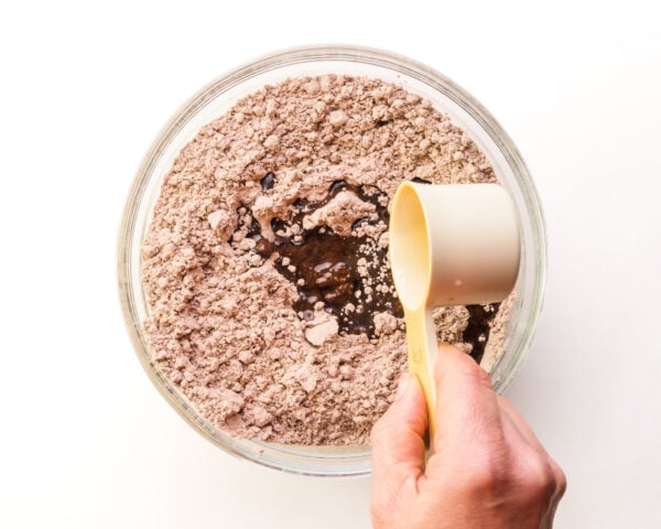 A hand holds a measuring cup pouring vegetable oil into a bowl witch chocolate brownie mix.