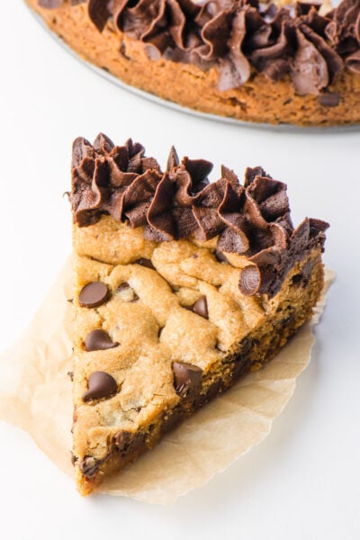 A slice of chocolate chip cookie cake on a napkin sits in front of the rest of the cake.