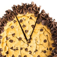 Cookie cake topped with chocolate frosting and chocolate chips, cut into slices.
