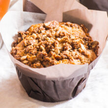 A coffee cake muffin sits next to a cup of hot tea.