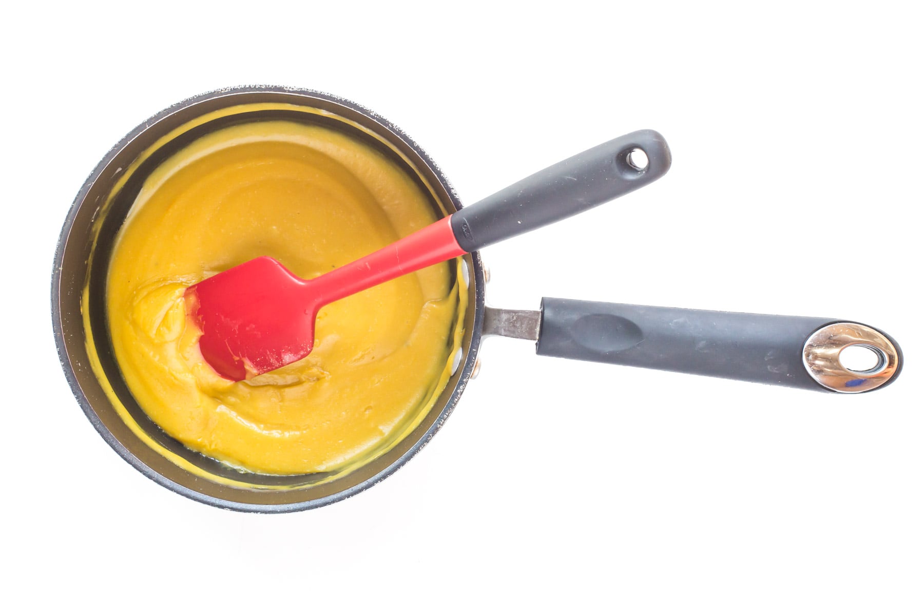 Looking down on sauce in a saucepan with a red spatula in it.