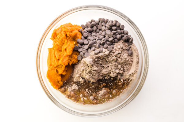 Ingredients are in a mixing bowl, including pumpkin puree, a brownie mix, chocolate chips, and vegetable oil.