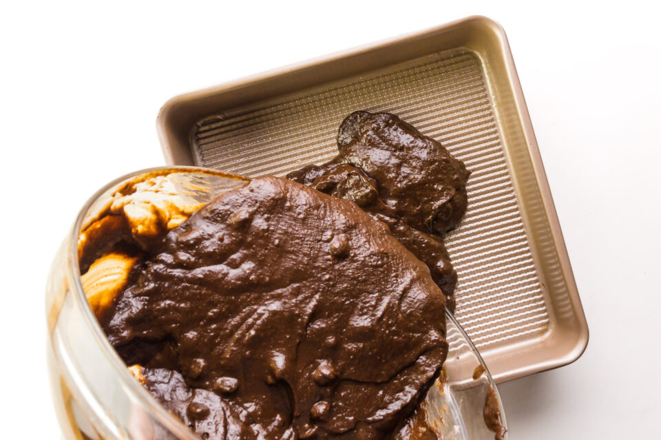 Chocolate brownie batter is being poured into a baking pan.