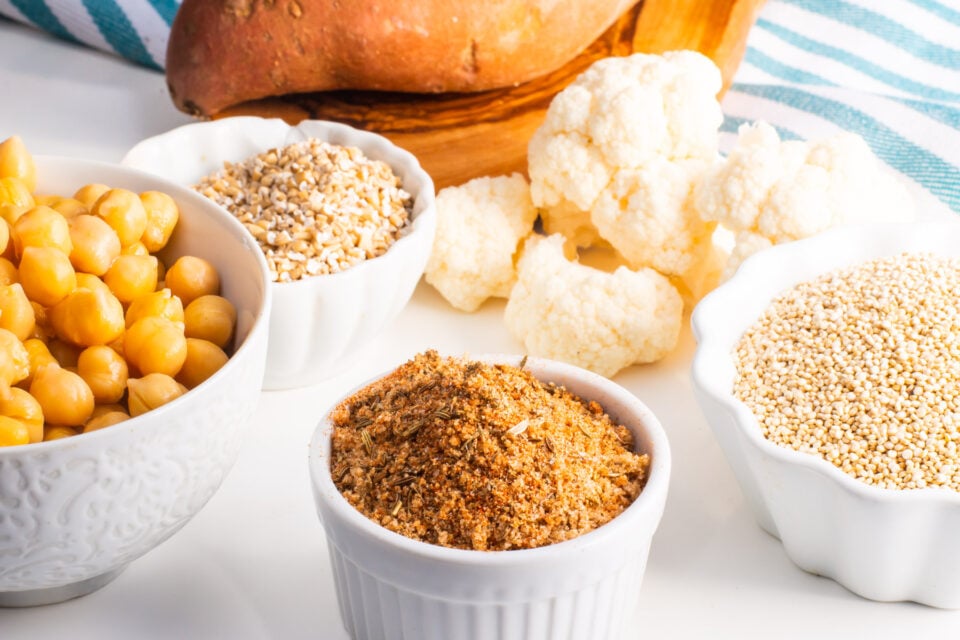 A bowl of spices sits beside bowls of chickpeas, grains, and other vegetables.