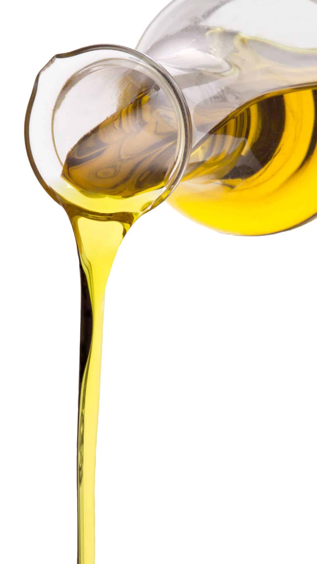 Olive oil is being poured from a glass pitcher.
