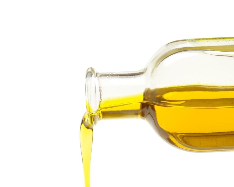 A side view of olive oil in a glass pitcher being poured.