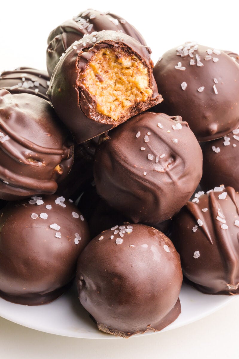 A stack of cashew butter balls sits on a plate. The top ball has a bite taken out.