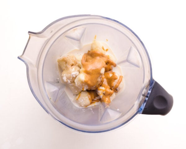Looking down on a blender with frozen banana slices topped with peanut butter.