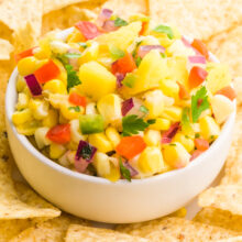 A bowl of mango corn salsa sits around tortilla chips.
