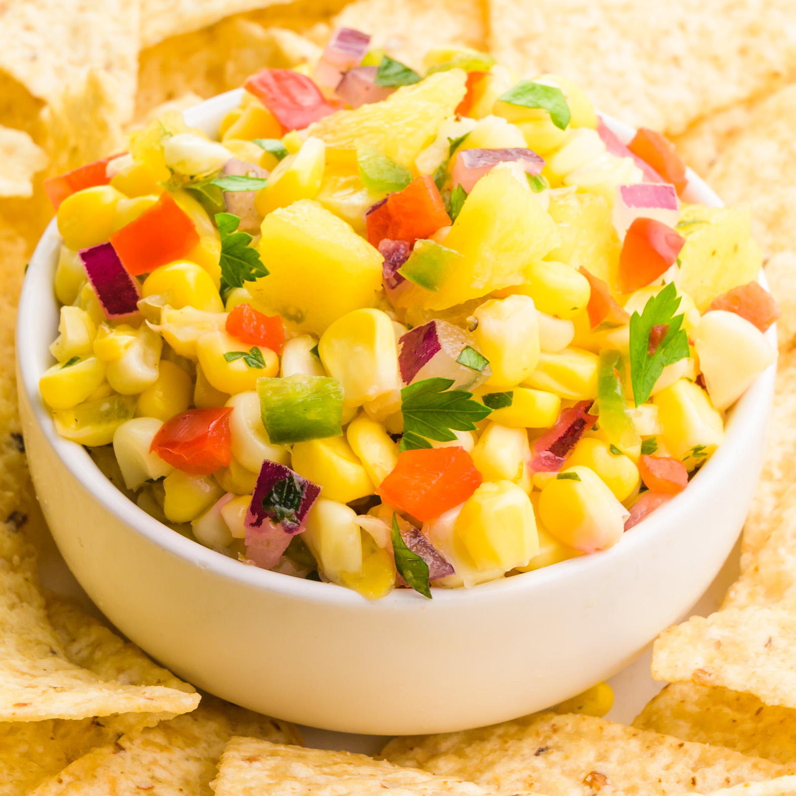 A bowl of mango corn salsa sits around tortilla chips.