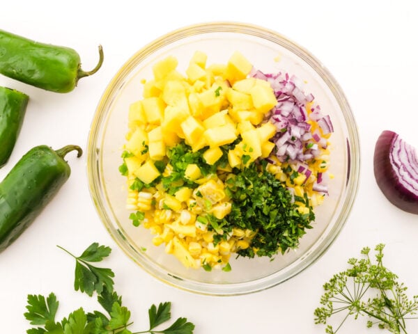 Looking down on a bowl with corn, chopped herbs, onions, mango, and more.