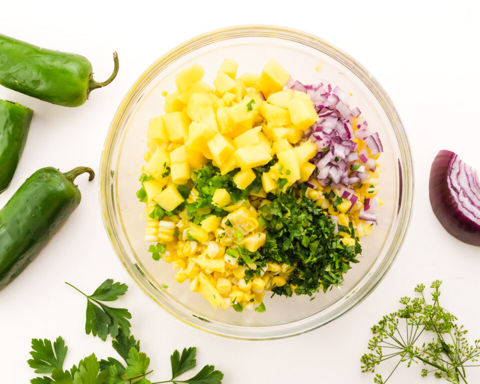 Looking down on a bowl with corn, chopped herbs, onions, mango, and more.