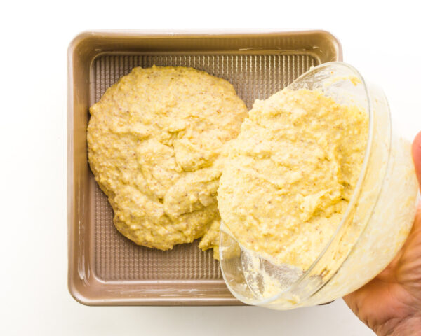 Cornbread batter is being poured into a square pan.