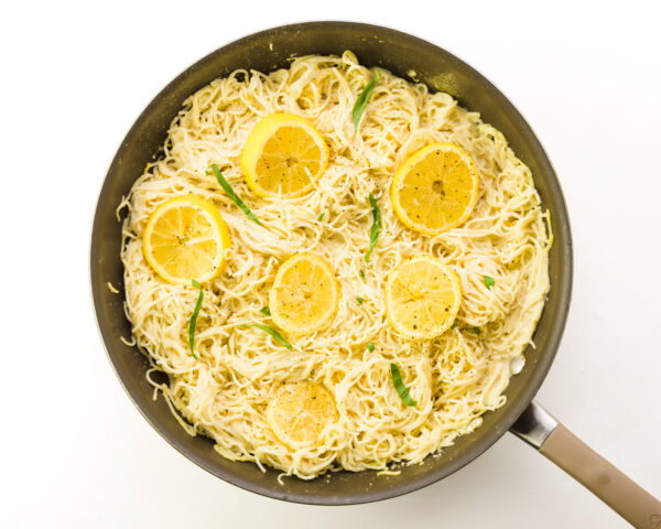 Looking down on lemon slices and basil on top of pasta in a pan.