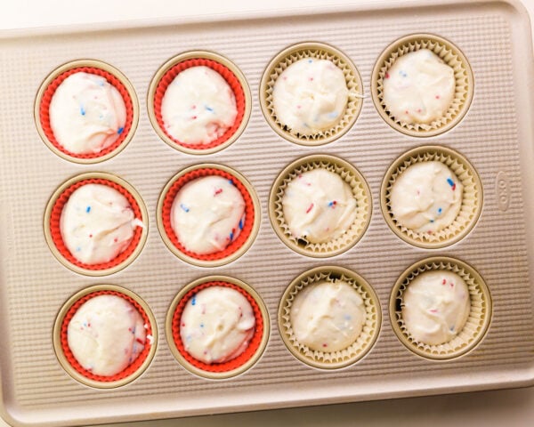 Looking down on a muffin pan with paper and silicone liners filled with cupcake batter.