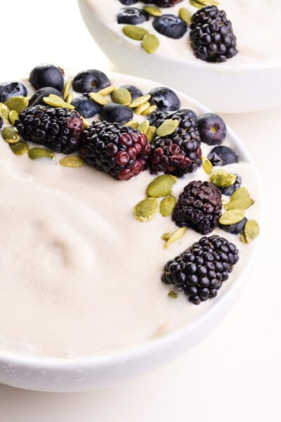 A closeup of a vanilla smoothie bowl with fresh fruit and pumpkin seeds on top. There's another bowl in the background.
