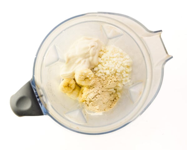 Looking down on ingredients like cauliflower and bananas in a blender jar.