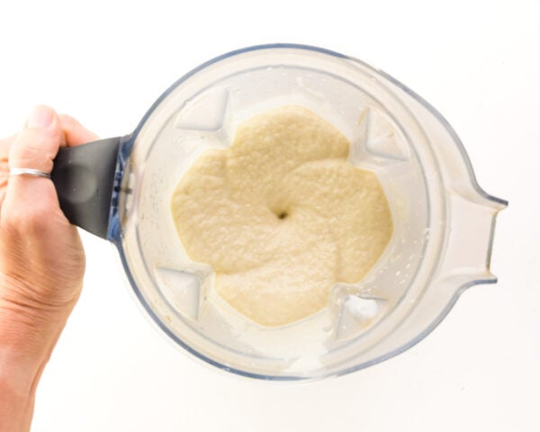 A hand holds a blender jar with freshly blended vanilla protein smoothie inside.