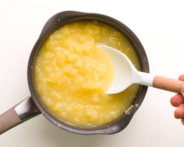 A spoon stirs a pineapple mixture in a saucepan.