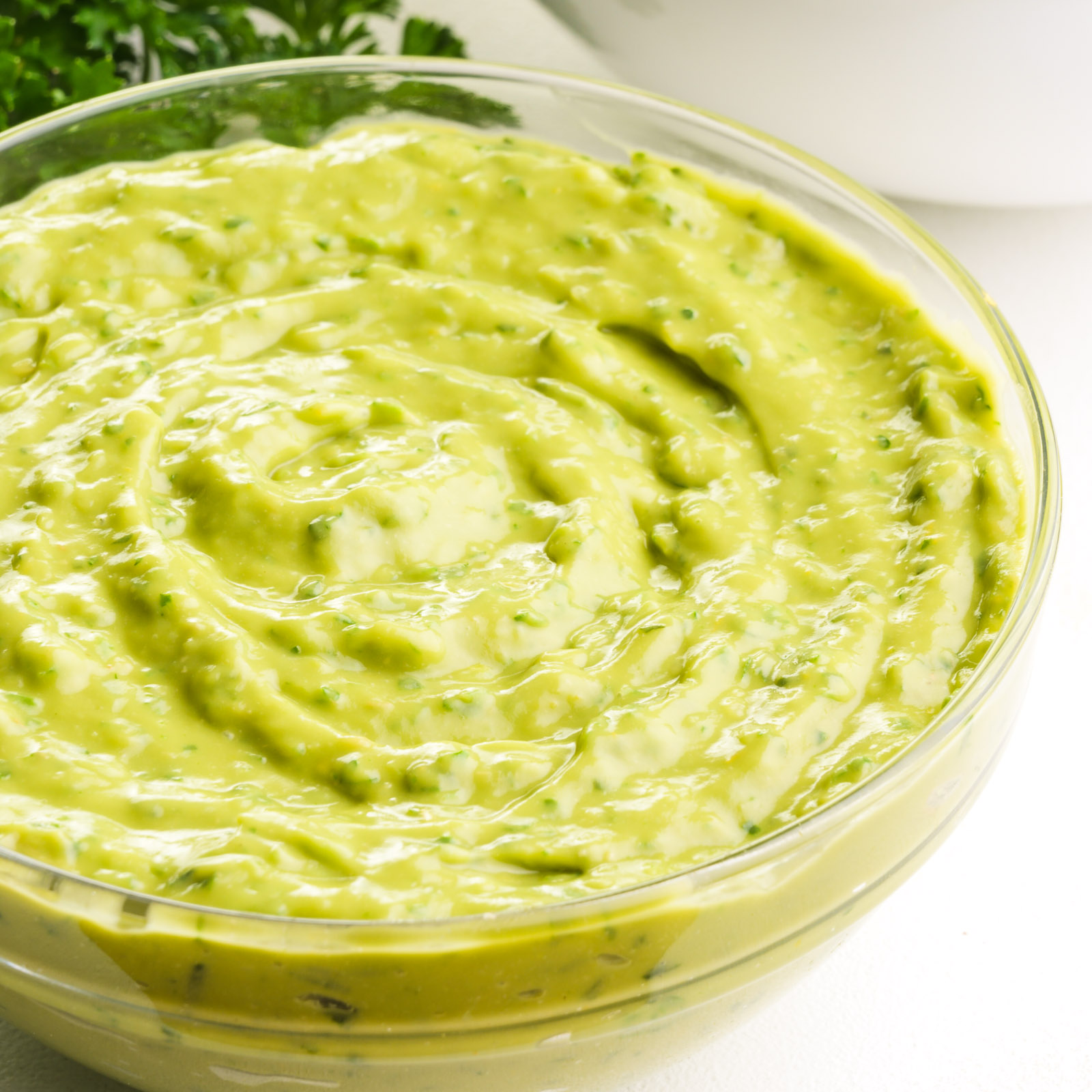 A bowl of fresh avocado green goddess salad dressing sits on a counter.