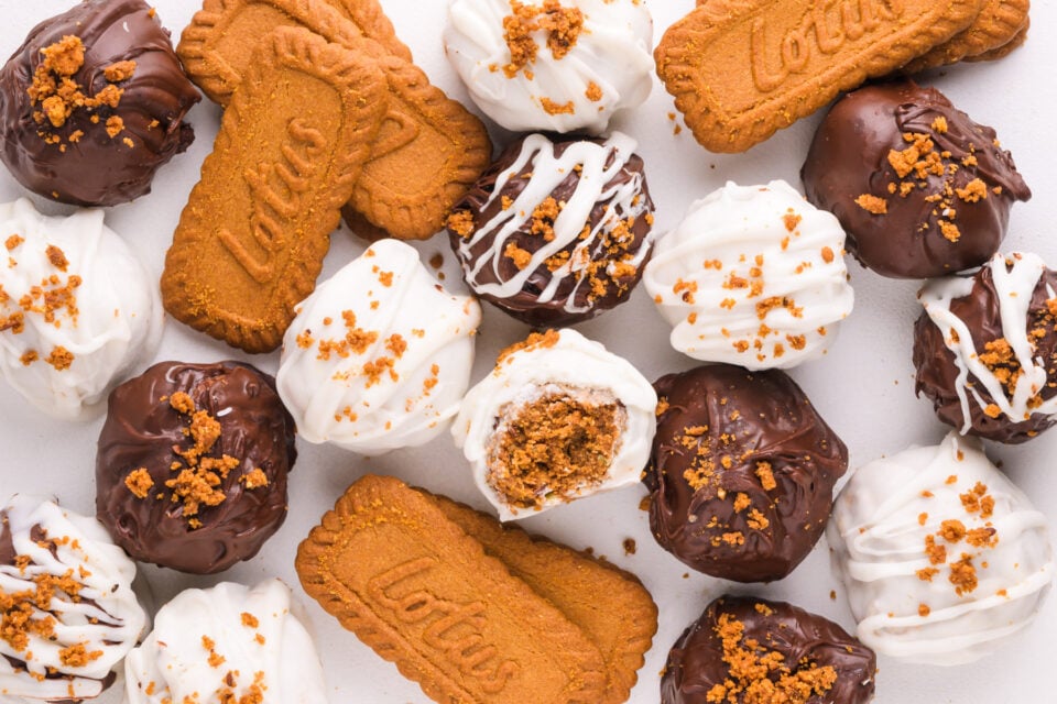 Looking down on white and dark chocolate truffles, one with a bite taken out. There are Biscoff cookies there too.
