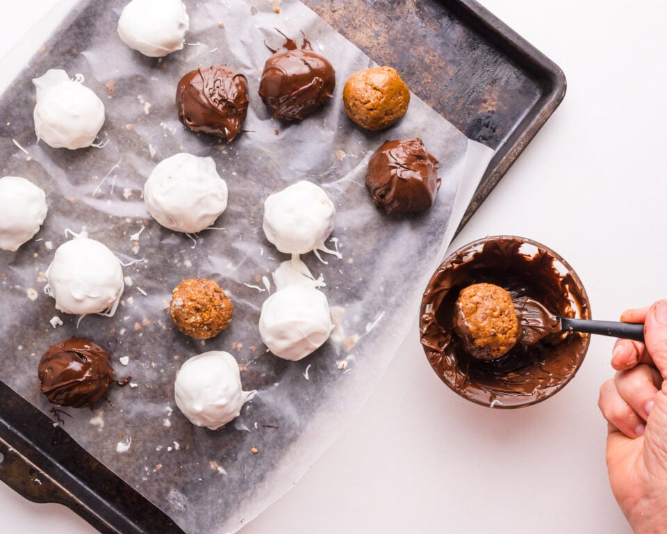 Looking down on a hand dipping truffles in melted chocolate. There is a pan with already dipped truffles sitting beside it.
