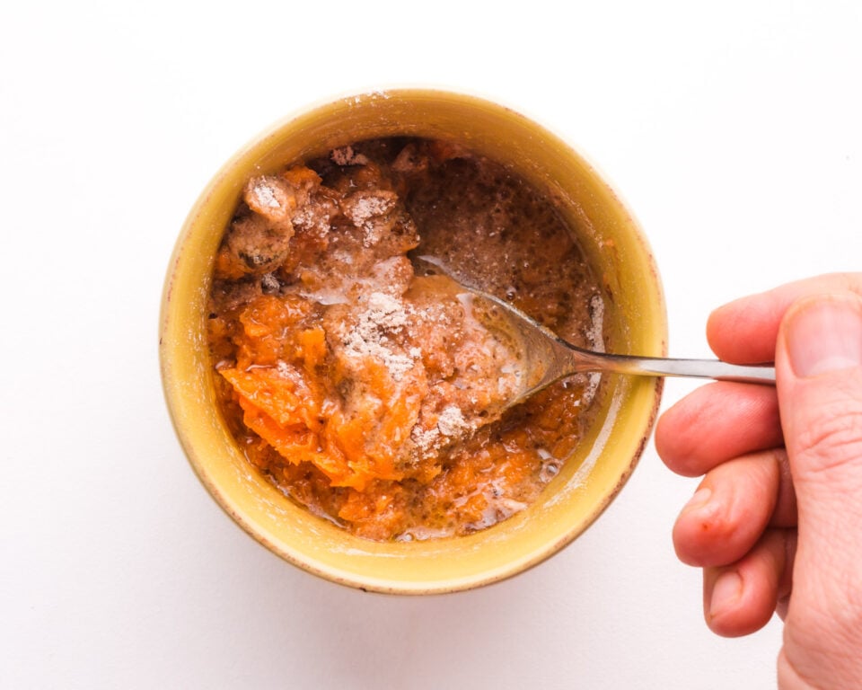 Looking down on a hand stirring carrot cake batter in a small dish.