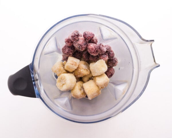 frozen cherries and bananas are in the bottom of a blender jar.