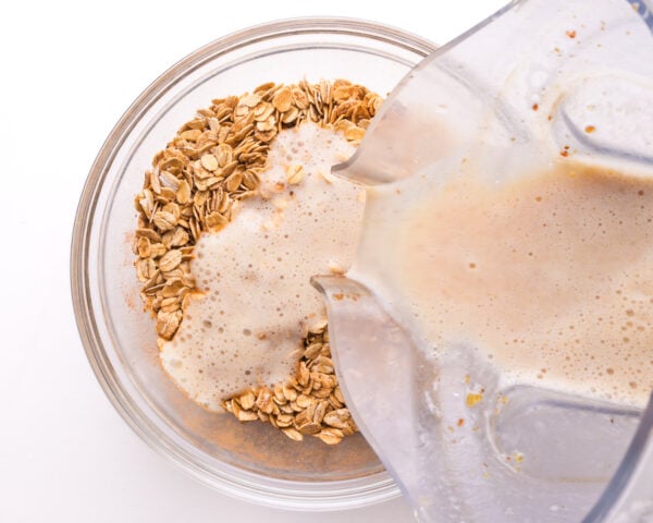A milk mixture is being poured from a blender into a bowl with oats.