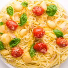 Looking down on a plate of pasta with roasted tomatoes and garlic. There is fresh basil on top, too.