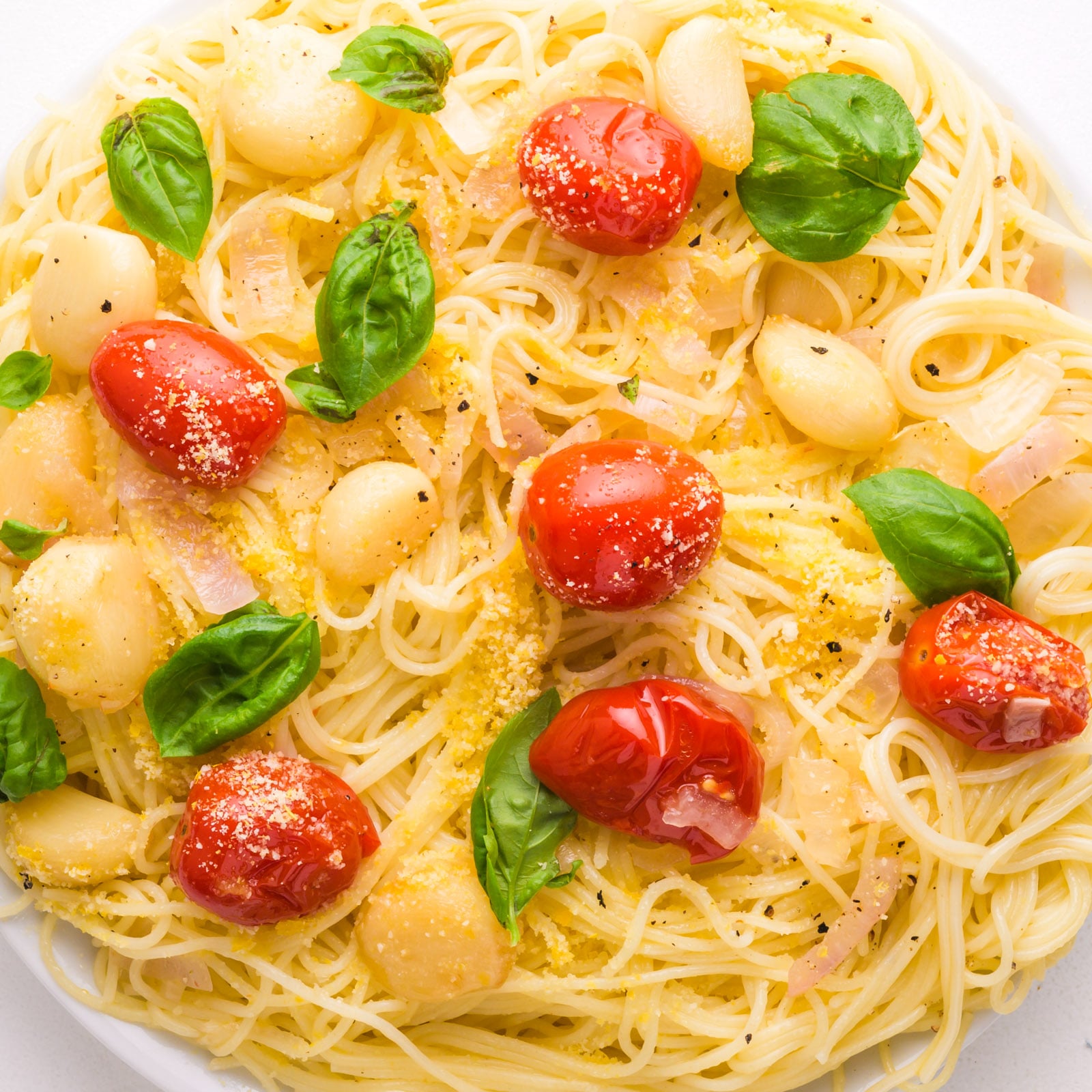 Looking down on a plate of pasta with roasted tomatoes and garlic. There is fresh basil on top, too.