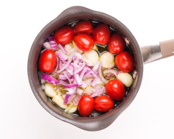 Tomatoes, garlic, and red onions are cooking in a saucepan.