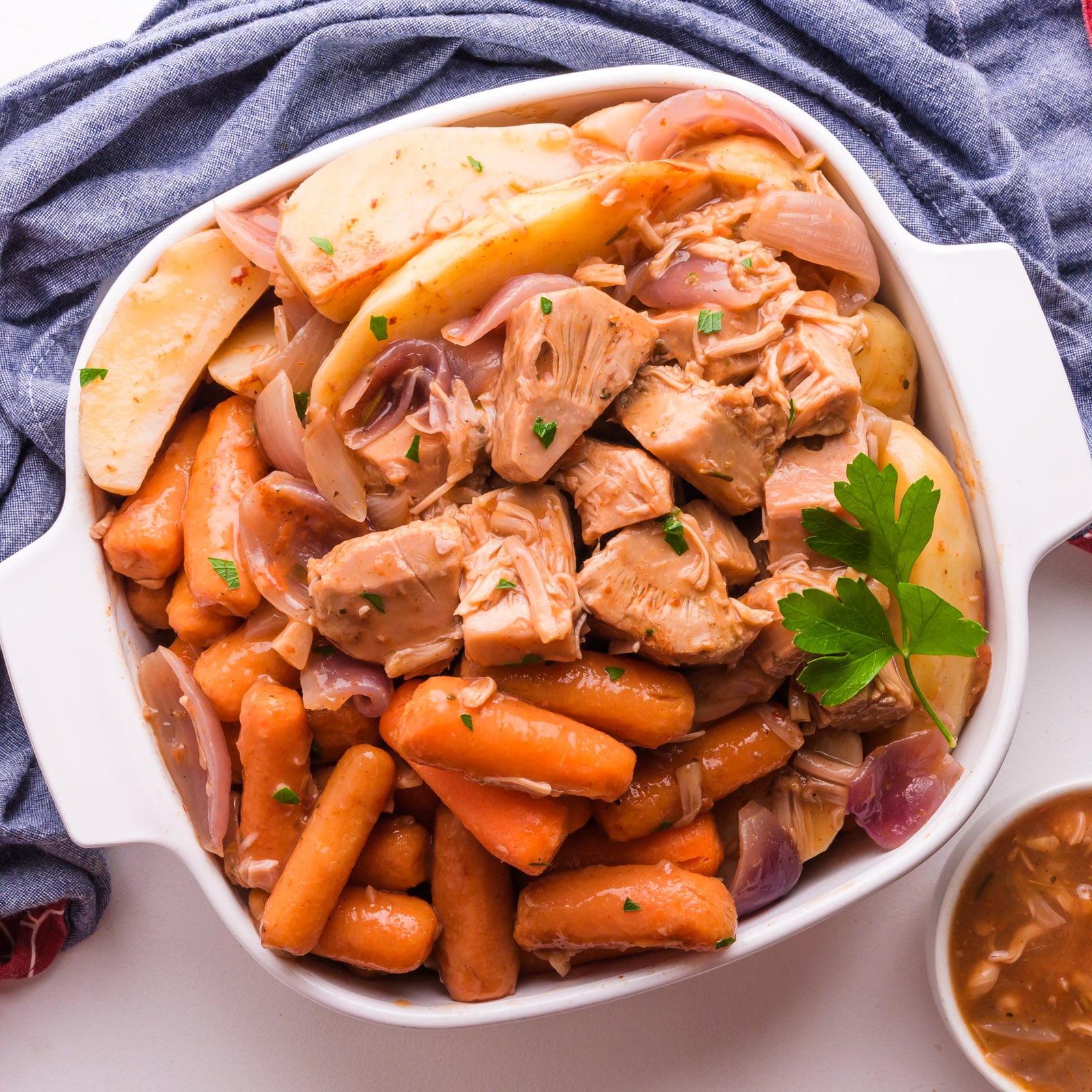 Looking down on jackfruit pot roast with potatoes and carrots in a baking dish.