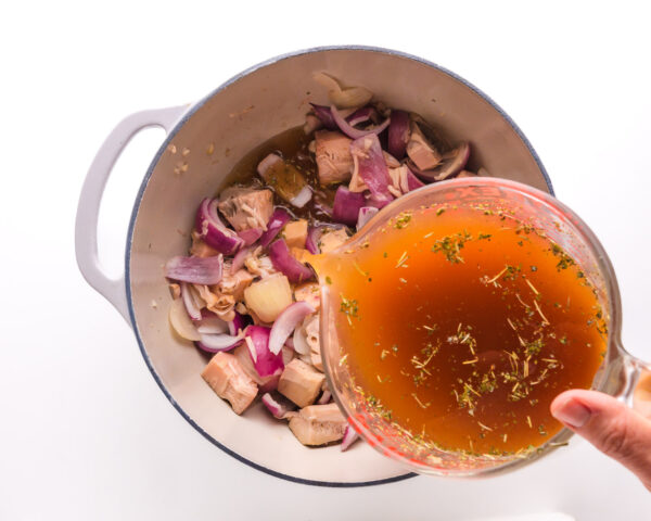 Vegetable broth is being poured into a pot with other vegetables and jackfruit.