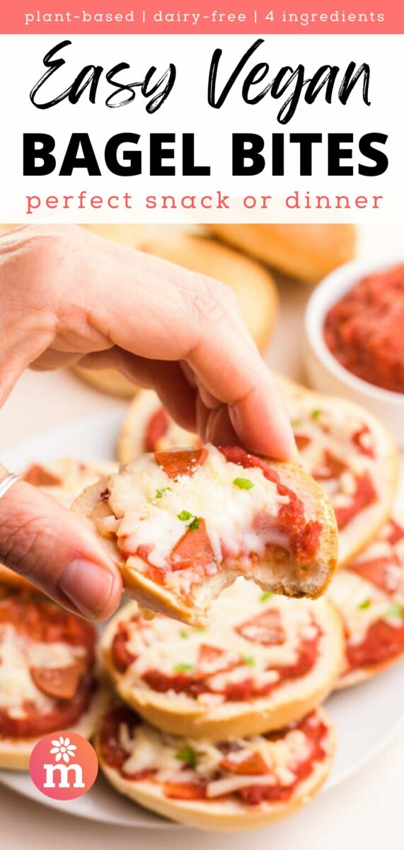 Vegan bagel bites topped with sauce and cheese, held by a hand, with more bagel bites in the background.