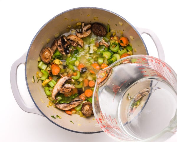 Water is being poured into a large pot with veggies.