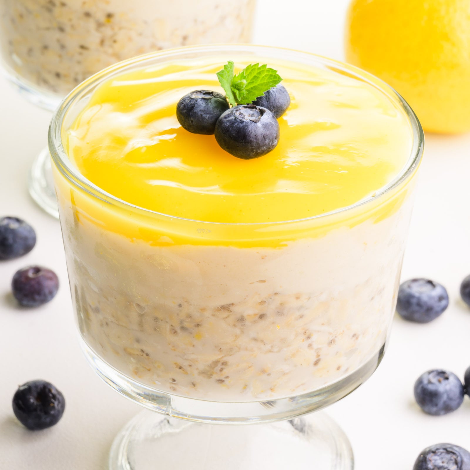 A bowl of lemon overnight oats is surrounded by fresh blueberries and a fresh lemon in the background.