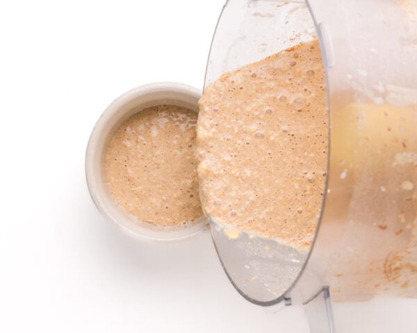 A batter is being poured from a food processor bowl into a ramekin.