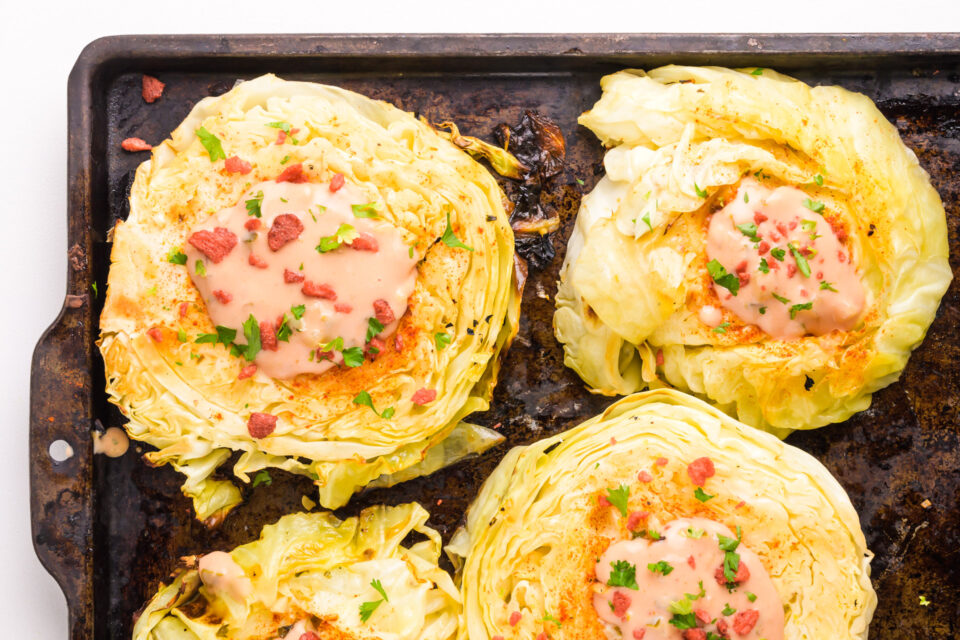 Looking down on cabbage steaks in a brown baking dish.
