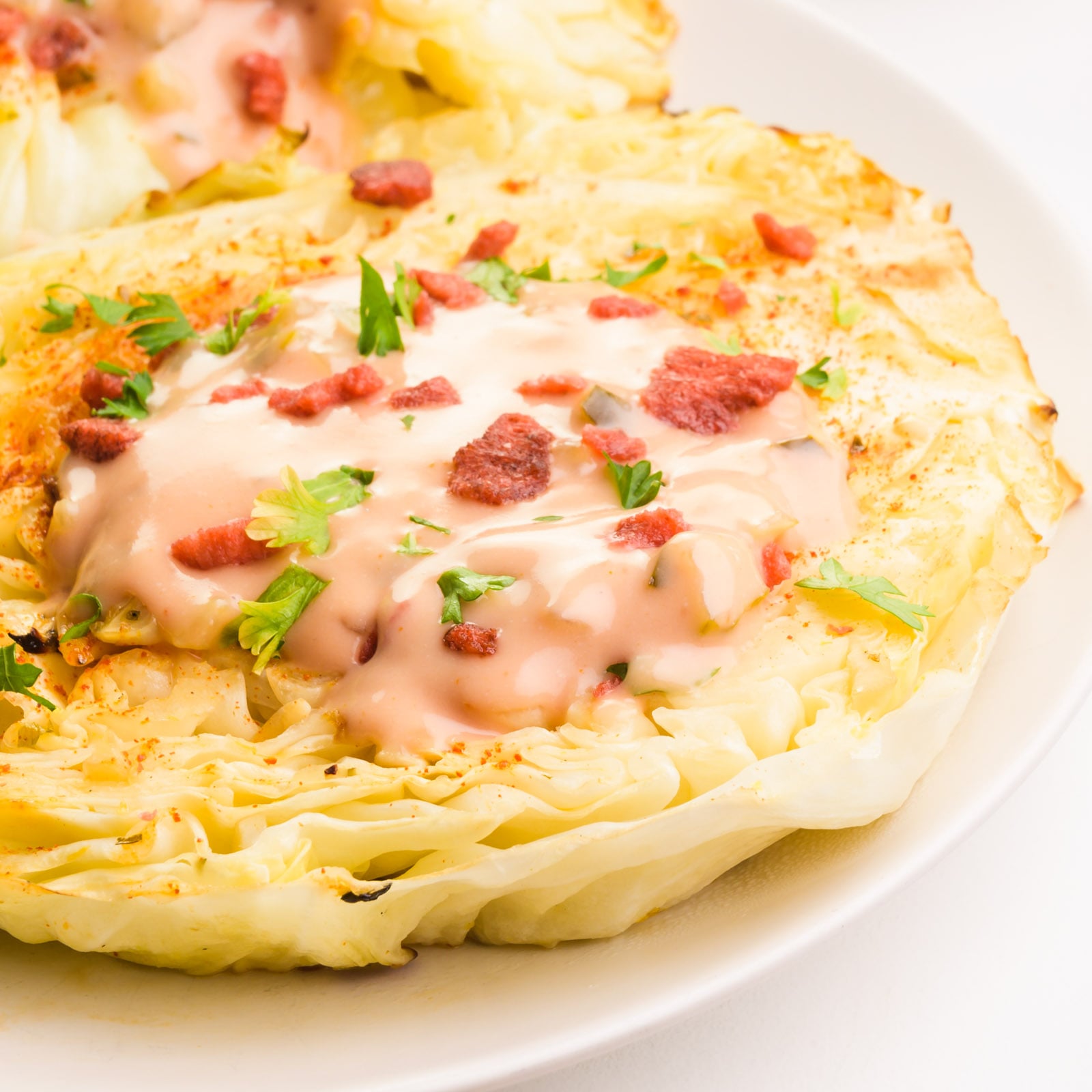 Cabbage steaks are sitting on a plate. They are topped with dressing and veggie bacon bits.