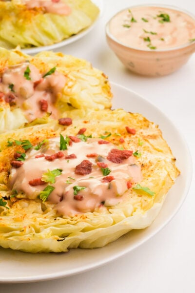 Cabbage steaks are displayed on plates next to a bowl of sauce.
