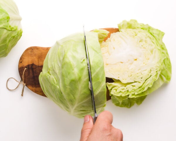 A hand uses a knife to cut cabbage in slices on a cutting board.