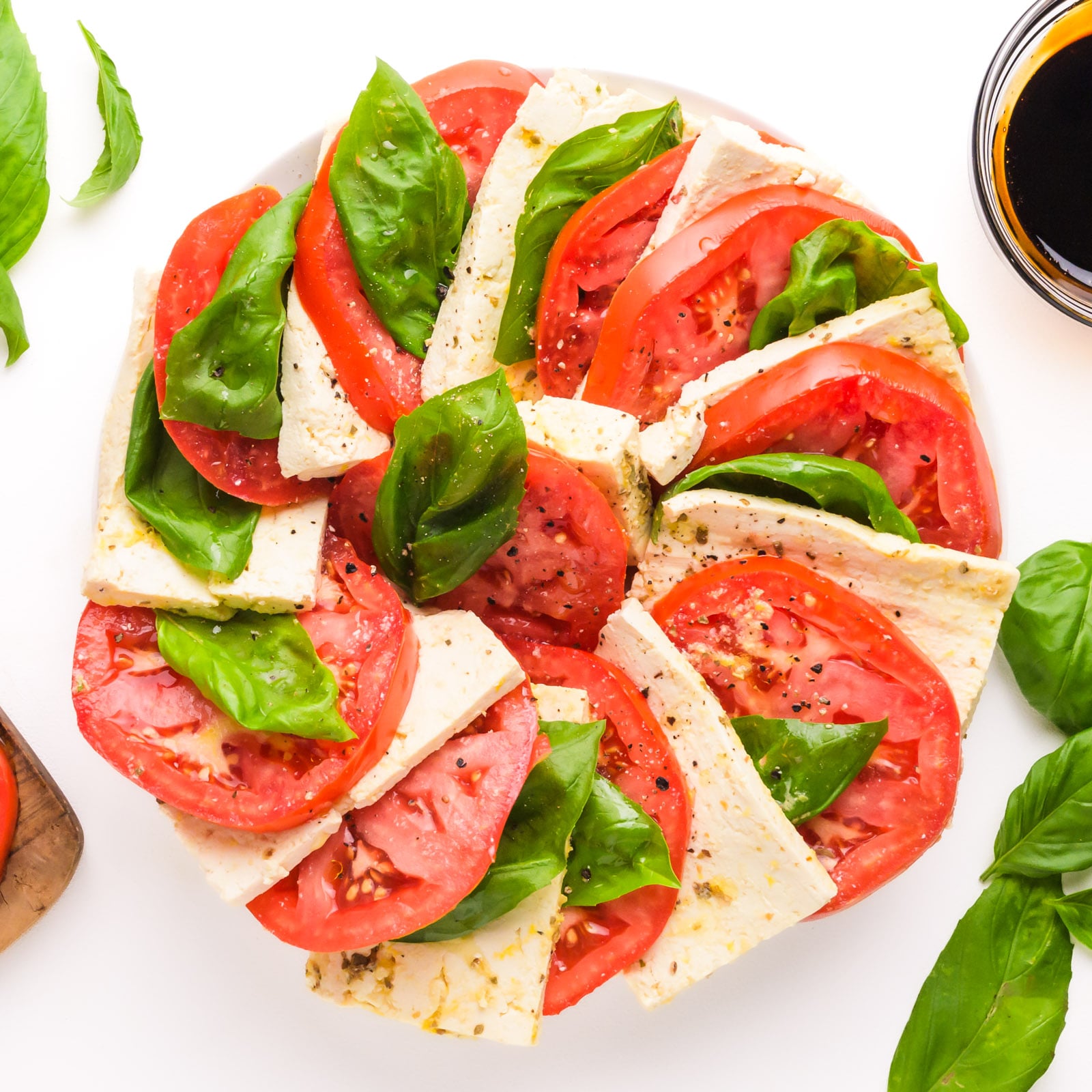 Looking down on a vegan Caprese salad with layers of tomatoes, tofu, and fresh basil.