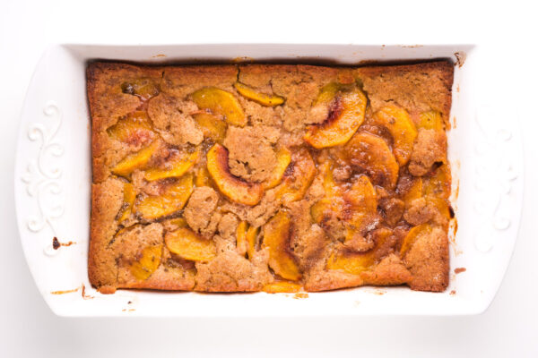Looking down on a cobbler in a baking dish. There are slices of peaches that have risen to the top of the baked dish.