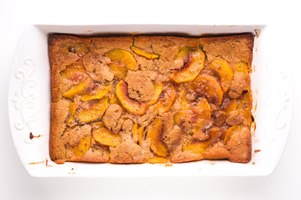 Looking down on a cobbler in a baking dish. There are slices of peaches that have risen to the top of the baked dish.